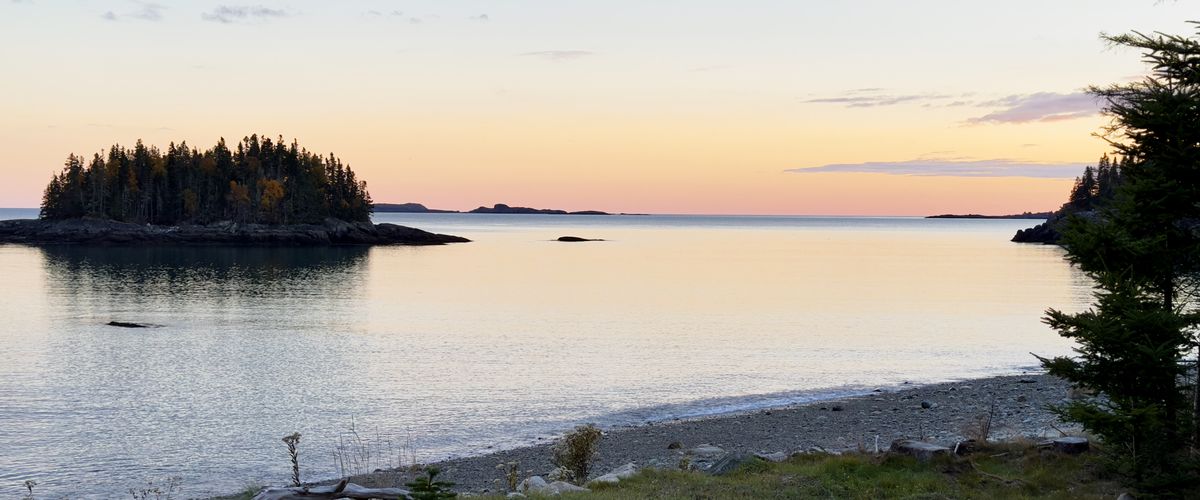 A wooded island in a still cove at sunset on the Maine coast